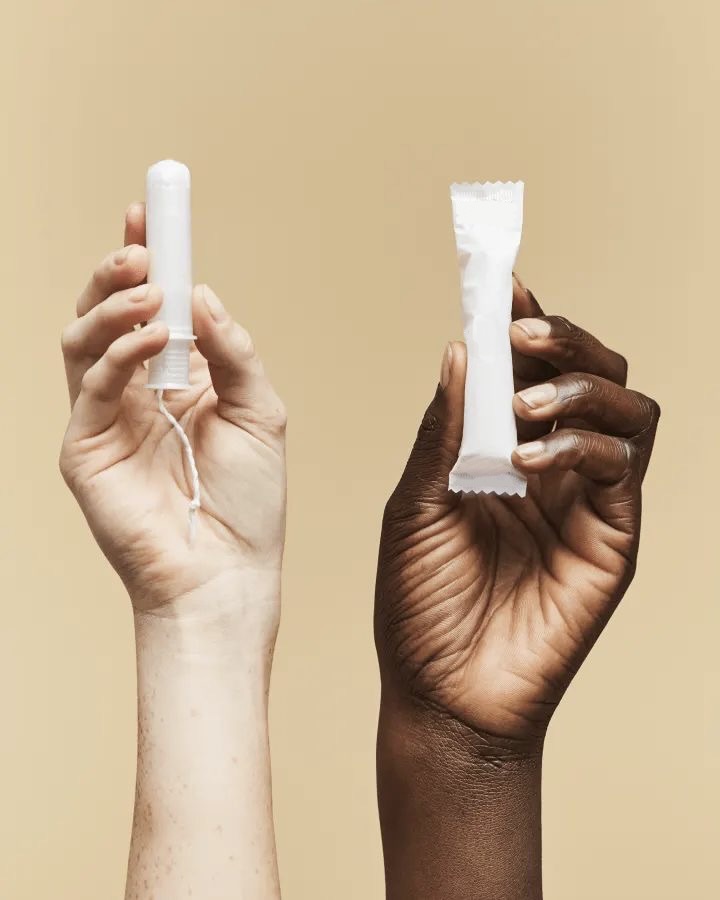 Two hands of different skin tones each holding a period product against a warm background